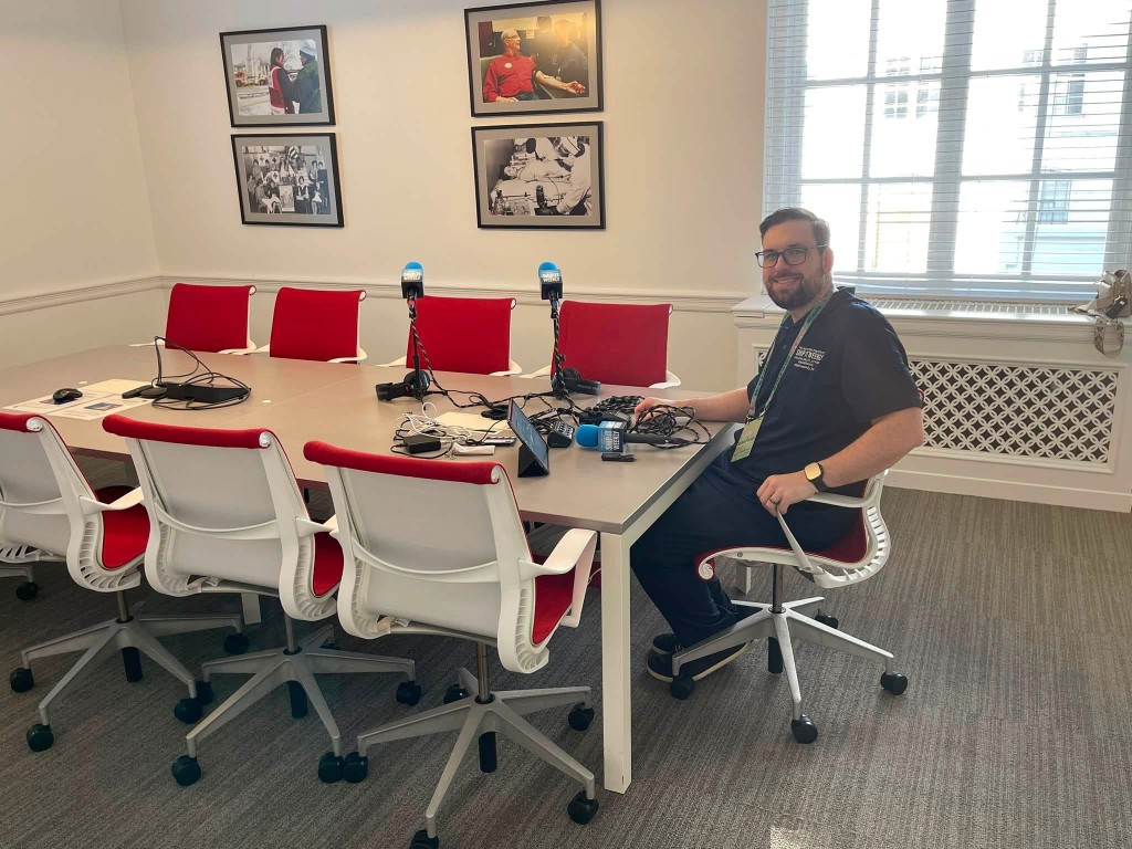 Brian Teller seated at the Ship It Weekly field kit while recording on site at DC State of the Stack 2026, with four microphones set up along a conference table at American Red Cross HQ.